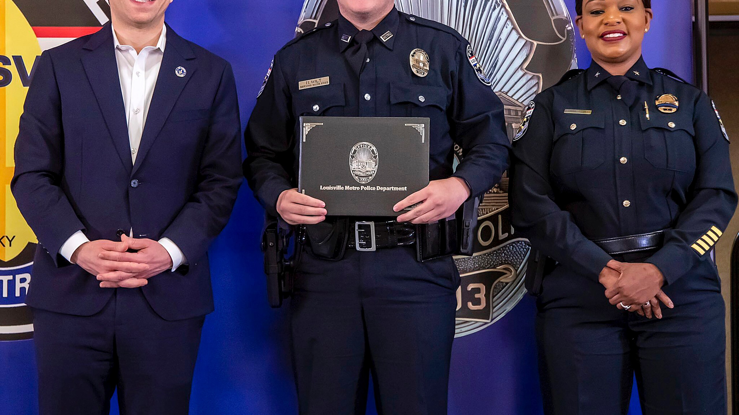 In this photo provided by the Louisville Metro Police Department, from left, Louisville Mayor Craig Greenberg, Officer Nickolas Wilt and Louisville Metro Interim Police Chief Jacquelyn Gwinn-Villaroel pose for a photo, in Louisville, Ky., March 31, 2023. Wilt was shot while responding to a call where a bank employee armed with a rifle opened fire at his workplace early Monday, April 10. (Louisville Metro Police Department via AP)