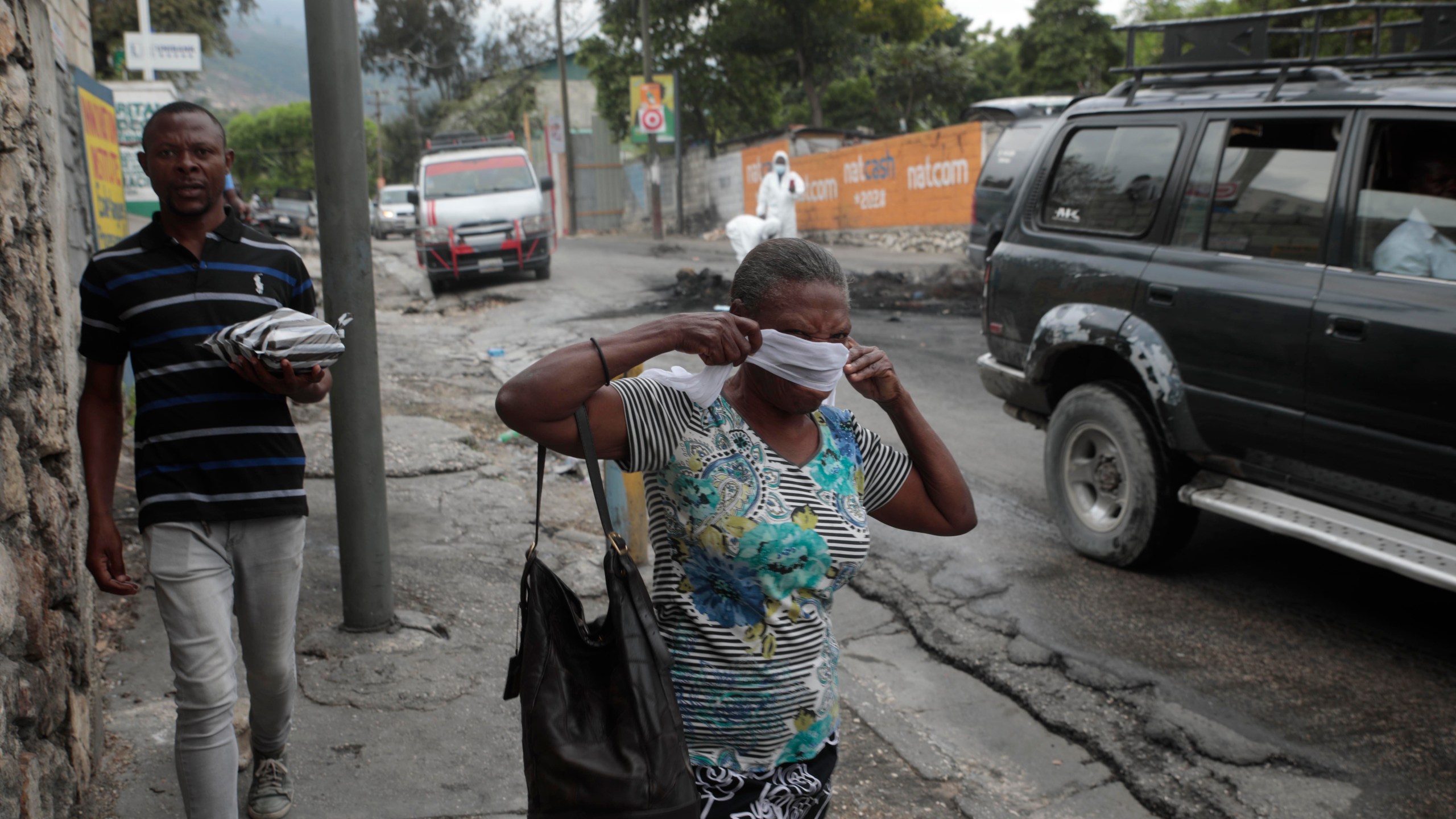 A woman walks past local authorities removing the bodies of men that were set on fire by a mob in Port-au-Prince, Haiti, Tuesday, April 25, 2023, a day after a mob pulled the 13 suspected gang members from police custody at a traffic stop and beat and burned them to death with gasoline-soaked tires. (AP Photo/Odelyn Joseph)