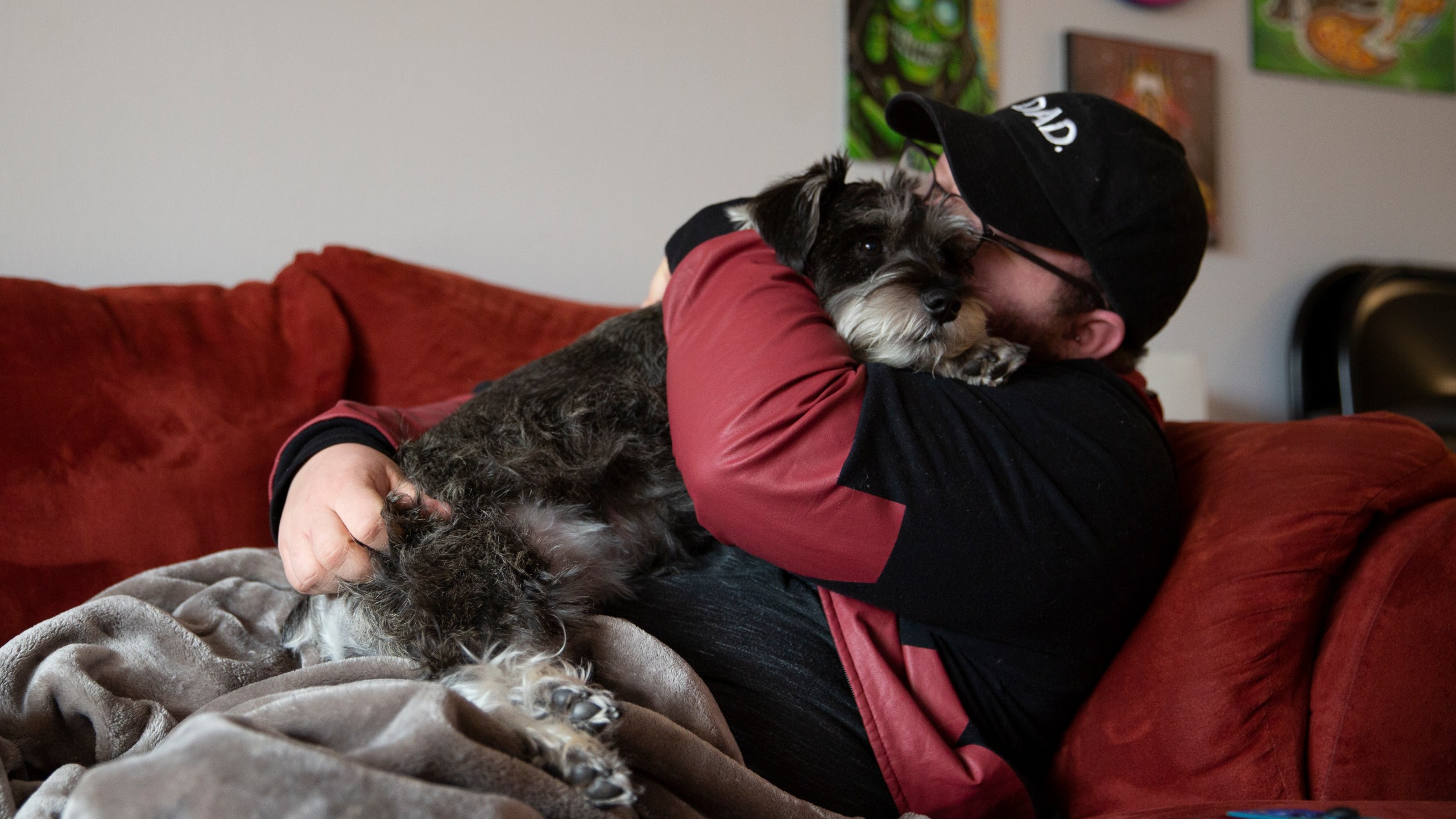 Eli cuddles his dog on the couch at his home in Casselberry, Fla., May 29, 2023. Eli and his fiancé Lucas, both transgender men, plan to move to Minnesota with their dog and two cats later this year. The Associated Press is not using Eli’s and Lucas’ last names because they fear reprisal. Minnesota is among the states this year that have codified protections for transgender people in response to sweeping anti-LGBTQ legislation in mostly Republican-led states. (AP Photo/Laura Bargfeld)