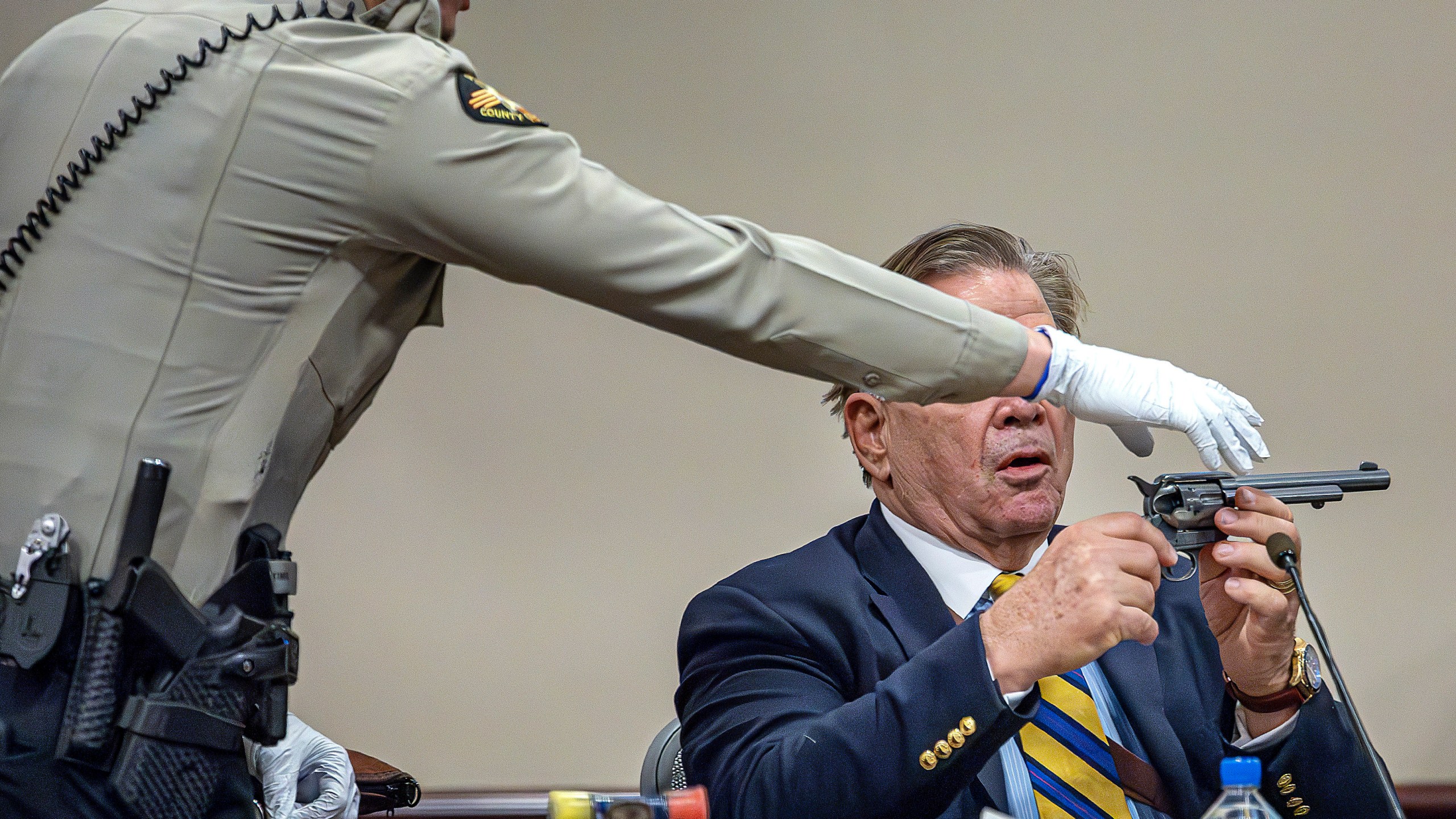 Santa Fe County Sheriffs Deputy Levi Abeyta, left, intervenes as a firearms expert for the defense, Frank Koucky III, points a replica gun in the direction of Judge Mary Marlowe Sommer while demonstrating how to remove the cylinder from a gun like the one used in the "Rust" shooting as Koucky testifies in the involuntary manslaughter trial of movie armorer Hannah Gutierrez-Reed, Tuesday, March 5, 2024, at the First Judicial District Courthouse in Santa Fe, N.M. (Jim Weber/Santa Fe New Mexican via AP, Pool)